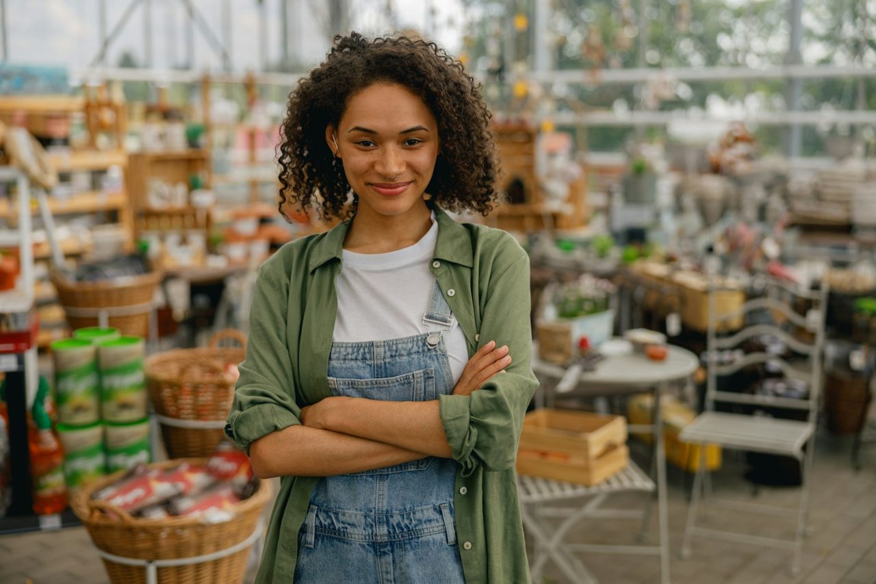 smiling-female-garden-shop-seller-standing-on-flower-store-background-gardening-concept.jpg